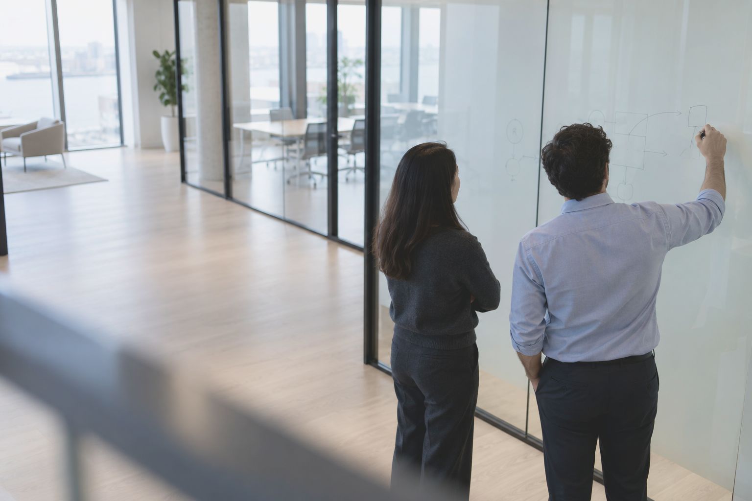 Two colleagues at a glass wall marked with a few hand drawn lines, seen from behind