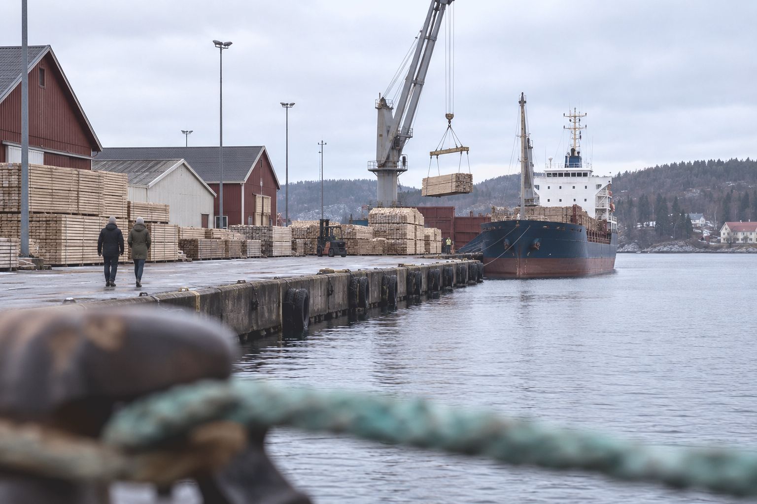 A Finnish harbour in late autumn, a cargo ship loading sawn timber beside red and white warehouses