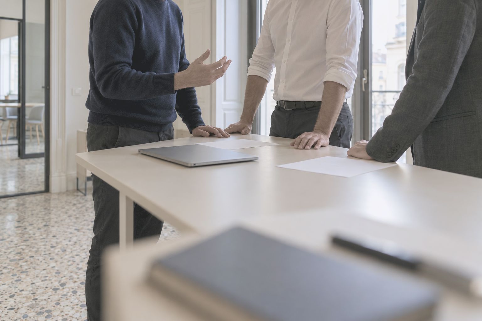 Three people talking over a standing desk, hands and papers in view