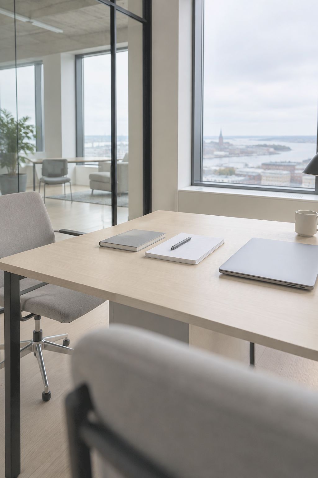 A desk by the window with notebooks and a laptop, in a quiet office